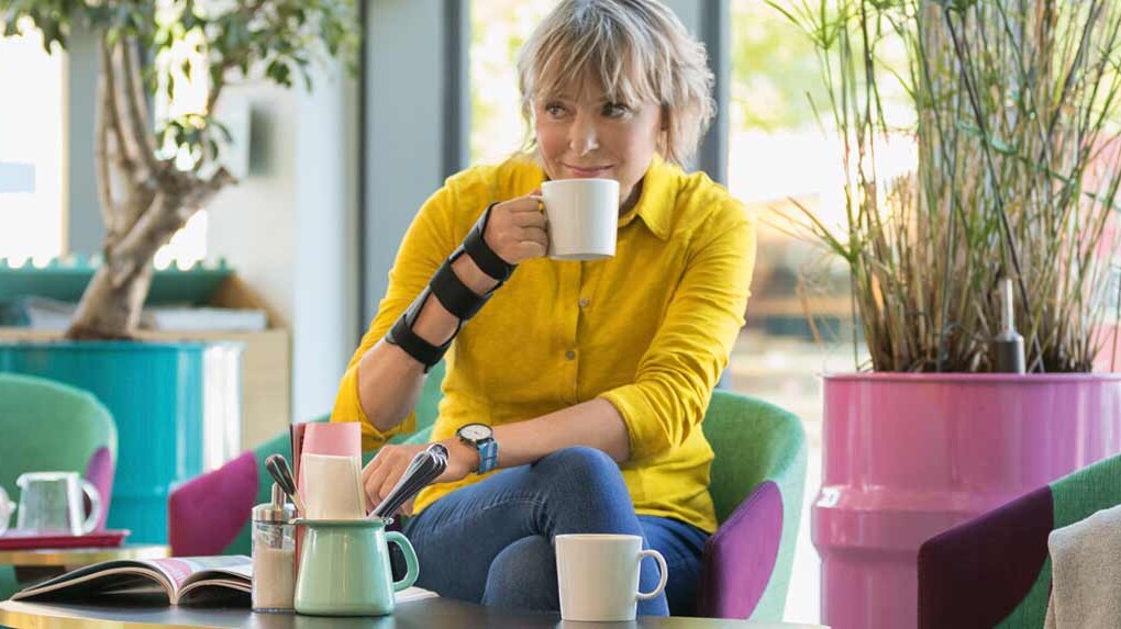 En kvinde bærer en JuzoPro Manu Xtec håndledsbandage og holder en kop i hånden