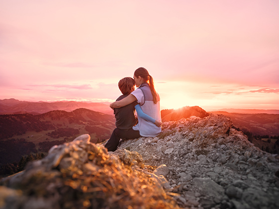 Scar Management A mother sits on a mountain peak with her child in her arms and watches the sunset.