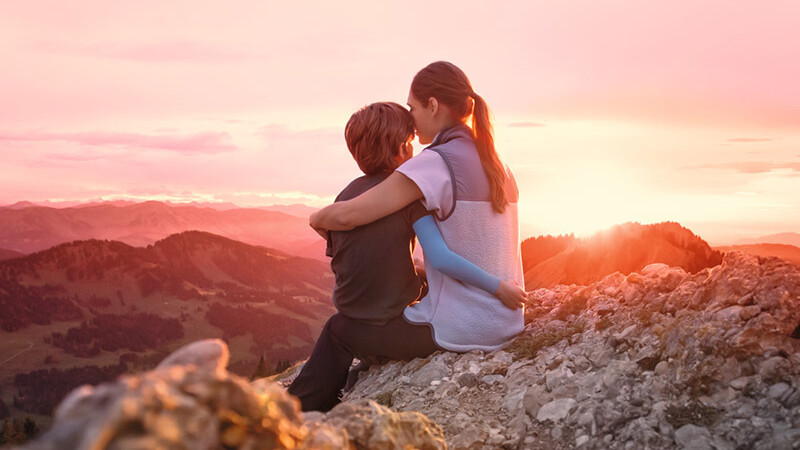 Una madre está sentada con su hijo en la cima de una montaña. El niño lleva una manga de compresión.
