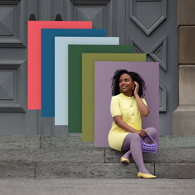 Juzo Trend Colours Batik A woman sits on stone steps in front of a gate. She wears a light yellow two-piece outfit with a purple compression garment. Behind her, you can see colour fields in the trend colours.