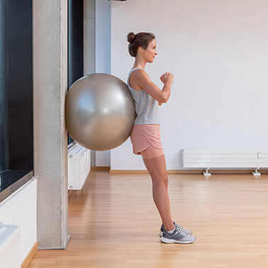 Frau lehnt sich aufrecht mit Gymnastikball an eine Wand Frau lehnt sich aufrecht mit Gymnastikball an eine Wand