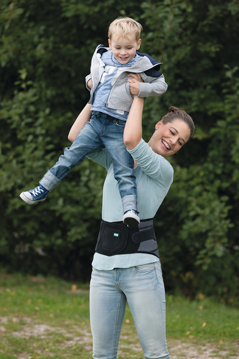 A woman is playing with her son. She is wearing a Juzo back brace. A woman is playing with her son. She is wearing a Juzo back brace.