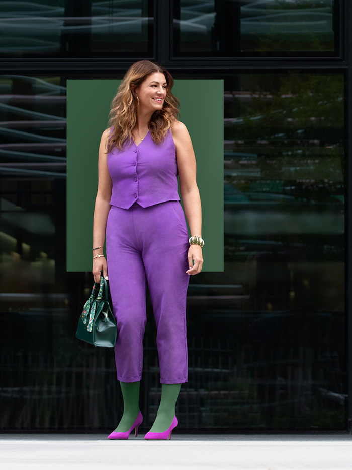 Strong Green A smiling woman in a purple two-piece outfit stands in front of a building wearing a Strong Green compression garment