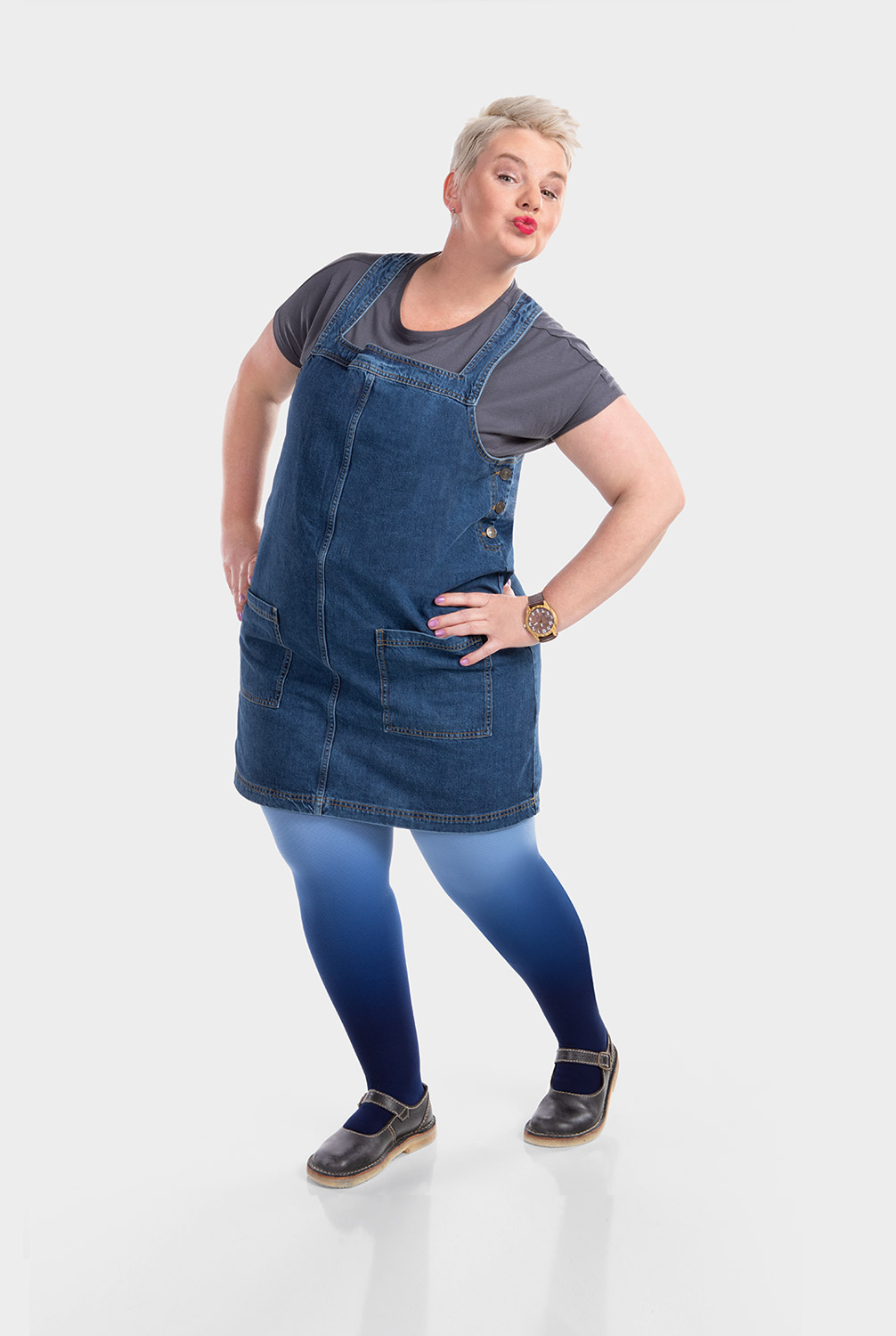 A woman is wearing a denim pinafore dress and compression hosiery in dip-dye blue
